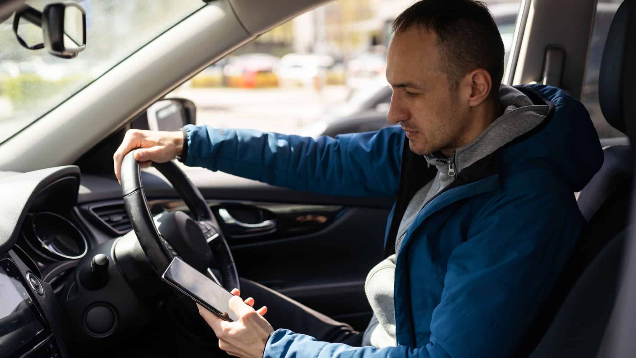Motorista de Uber em carro; homem segura volante com uma mão e celular com a outra