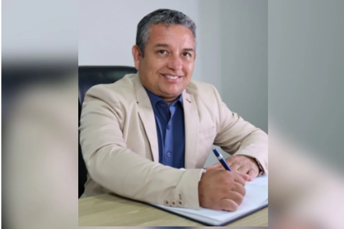 Imagens coloridas mostram prefeito de Pratânia (SP), Osmir Félix, homem branco, sentado, sorrindo de terno bege, camisa e gravata azuis
