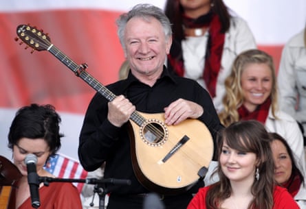 Musician Donal Lunny smiles before a crowd holding an stringed madolin-type instrument