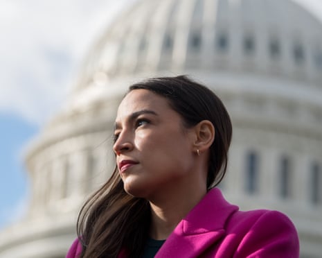 Alexandria Ocasio-Cortez, in a pink coat, gazes into the distance outside the US Capitol